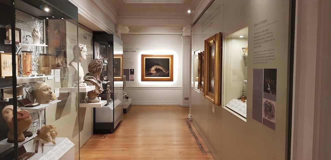 A series of displays line the muted white walls of the History of Surgery Museum. A oil painting with a thick frame is on the end wall.