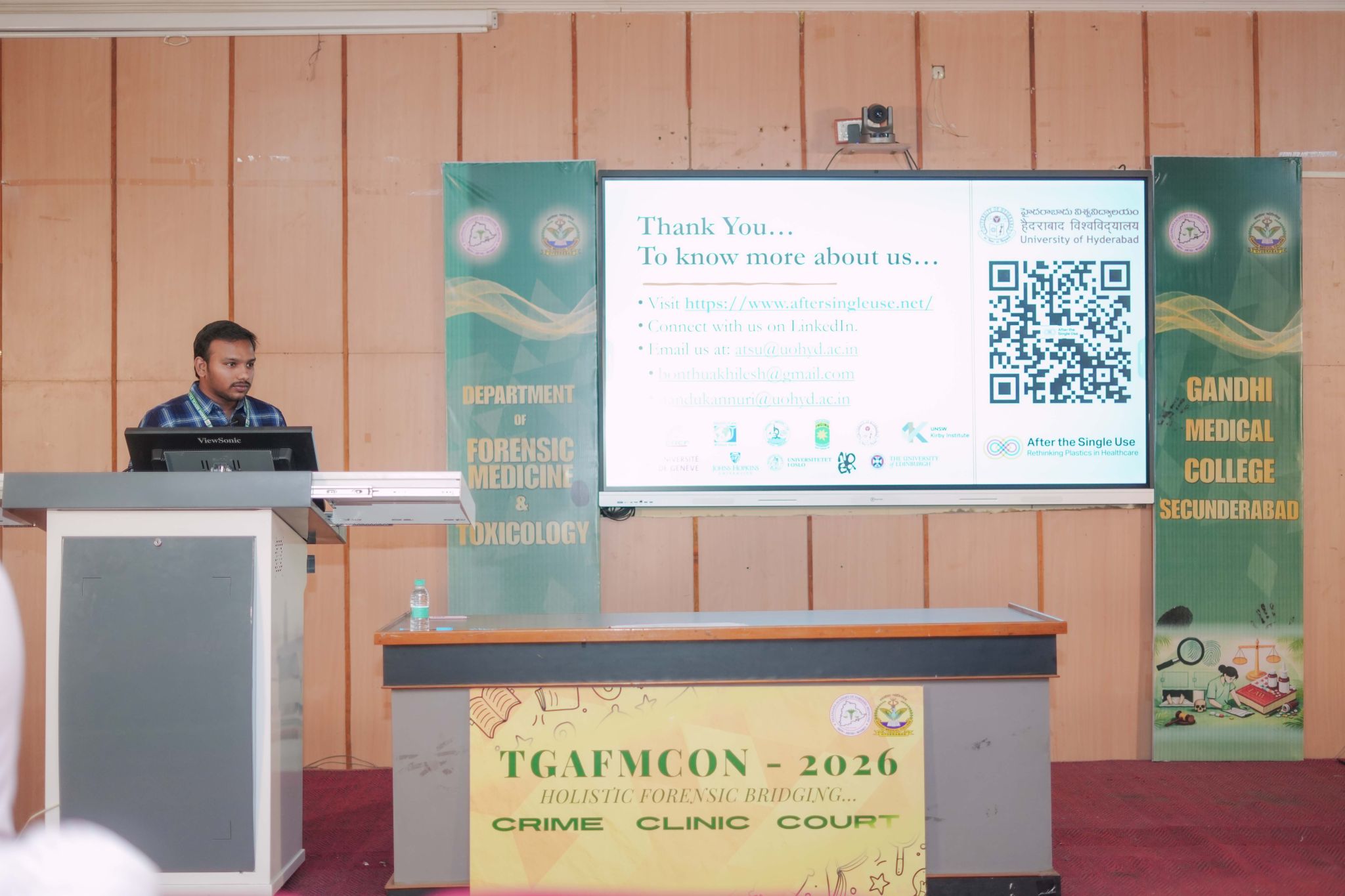 After the Single Use researcher Akhilesh Bonthu presenting a paper at a lecture in a room with wooden panelling behind him and a projector screen.