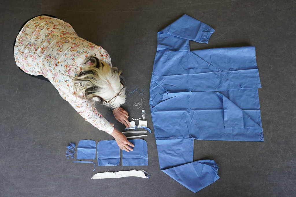 A researcher lays out the different white and blue materials found in a gown and mask on a grey floor.