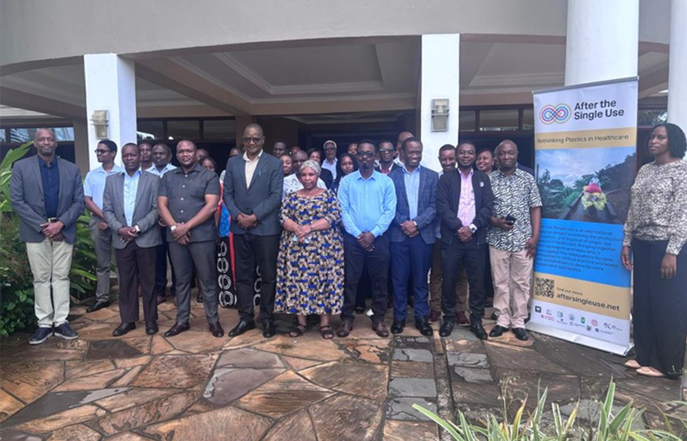 A group of attendees from the Tanga health sector and research community stand outside a building entrance with a banner at the right hand side.