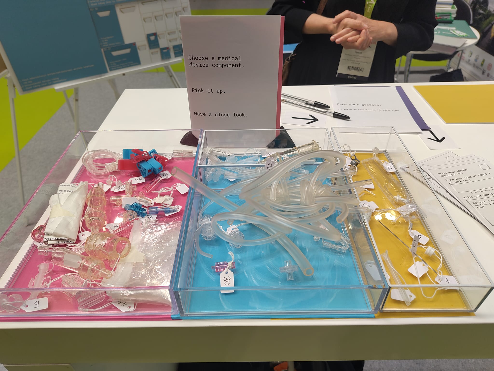 A table with 3 receptacles with deconstructed plastic medical devices that are labelled with a series of forms by the side of them. 