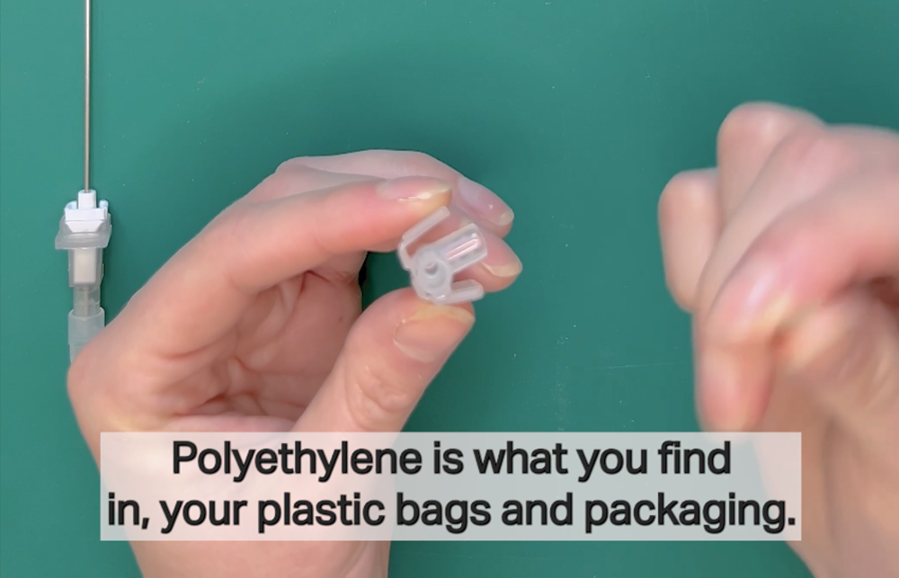 A pair of hands hold plastic parts of an IV catheter against a green background with subtitles from the video. 