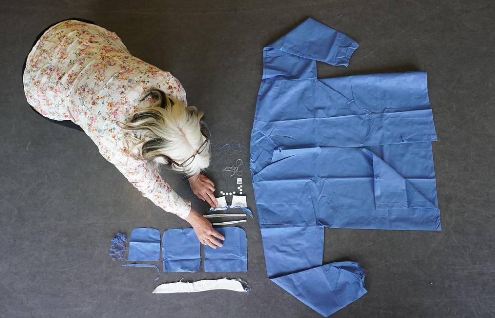 A researcher lays out the different white and blue materials found in a gown and mask on a grey floor. 