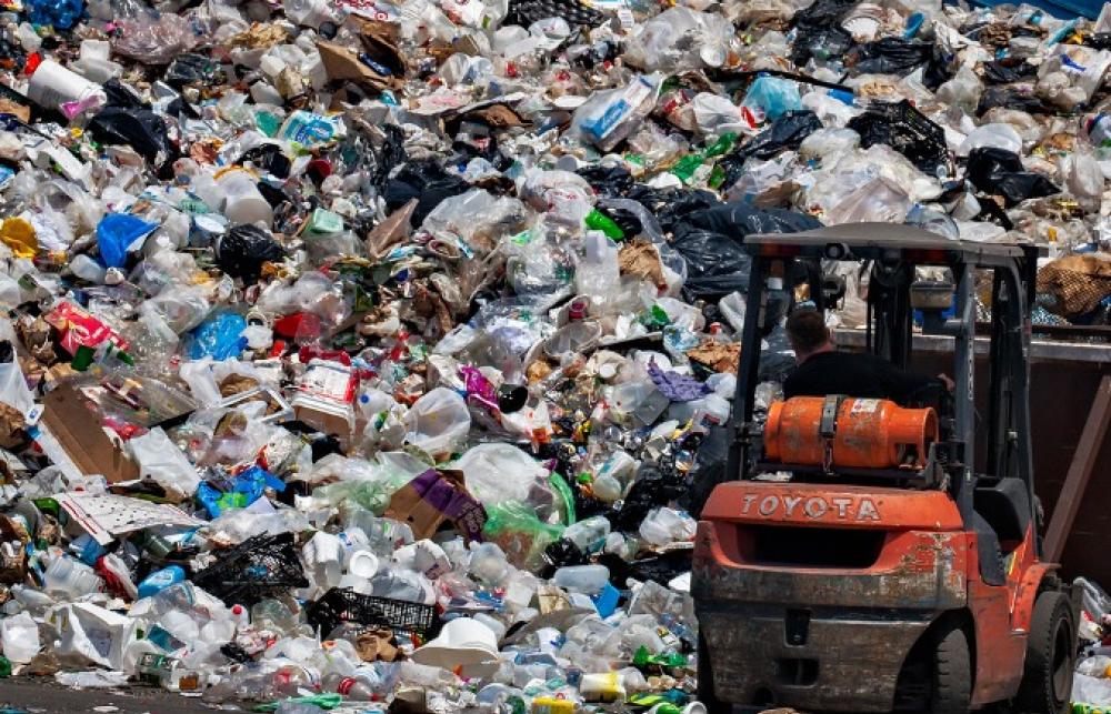A large wall of waste is being moved around by an orange forklift truck digger. 