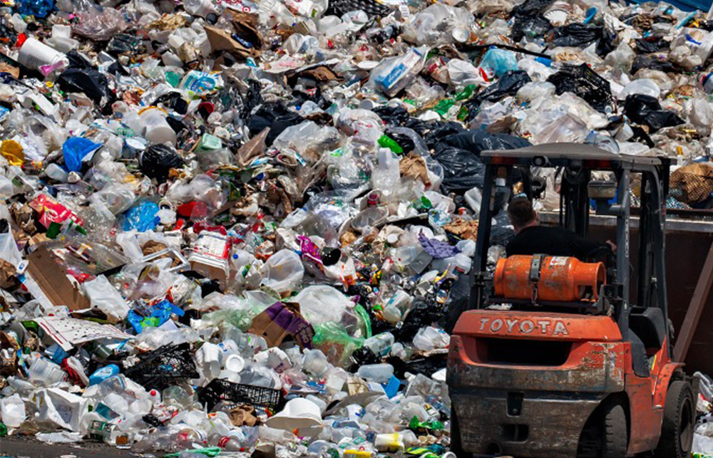 A large wall of waste is being moved around by an orange forklift truck digger. 