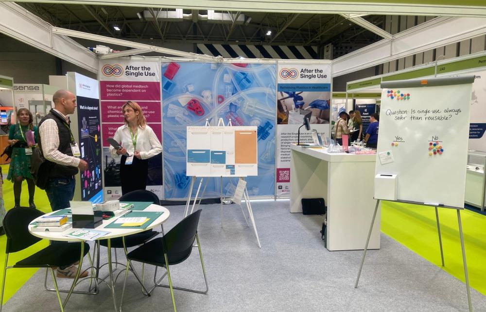 A conference exhibition space is shown with two people engaging in conversation and tables and displays showing the After the Single Use project. 
