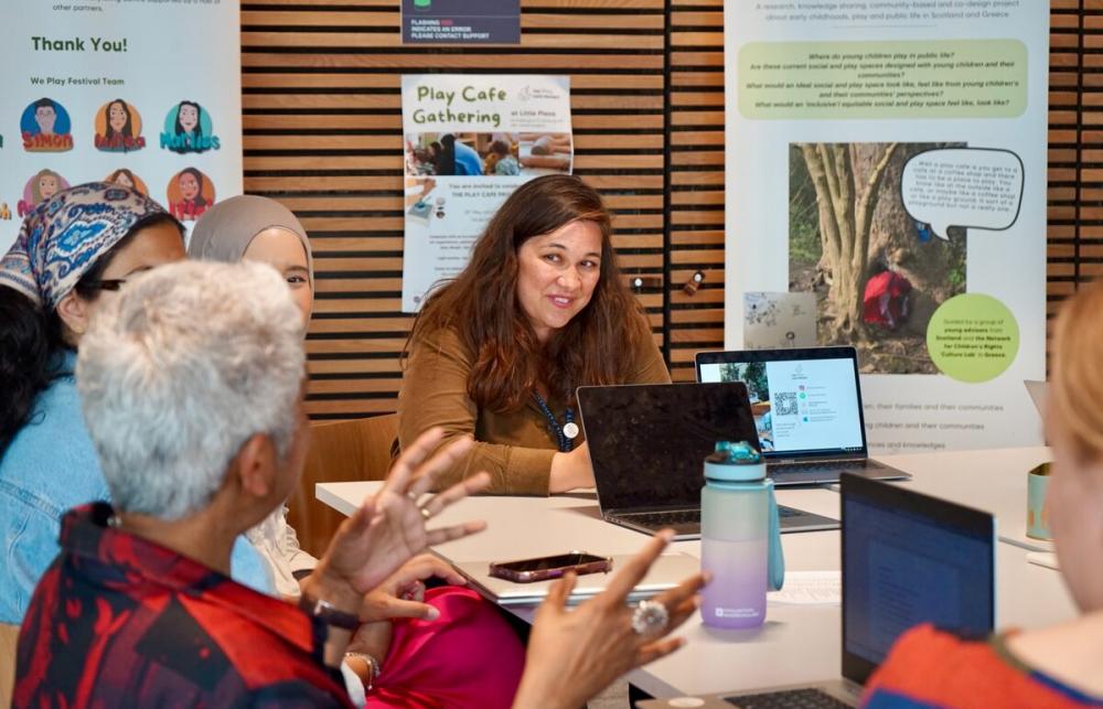 A lively workshop over a table with infographics in the background. One participant is smiling and listening intently to another participant talking. 