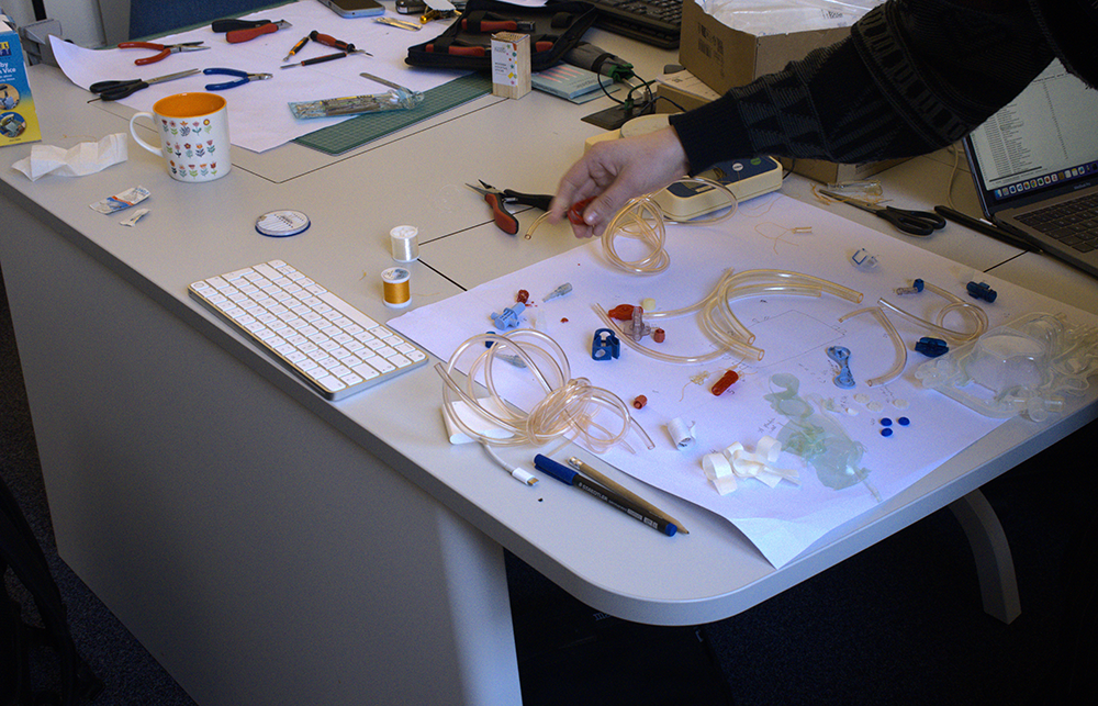 on a white desk with small tools some plastic medical devices are taken apart into components with an arm in frame