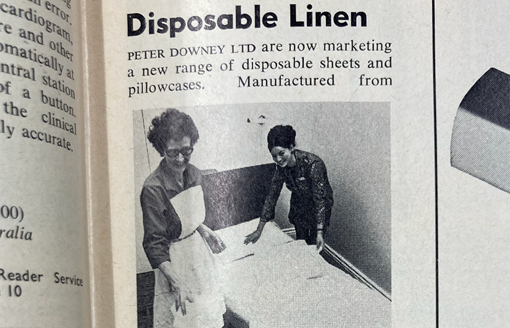 A black and white advert for disposable linen has two medical staff changing sheets on a bed. 