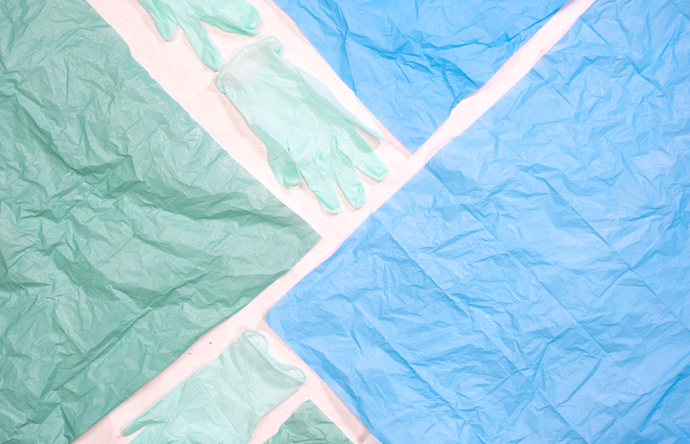 Blue and green plastic gloves and medical sheets are laid on a table.